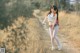 A woman walking down a dirt road in a field.