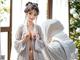 A woman in a white kimono standing in front of a window.