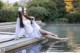 A woman in a white dress sitting on the edge of a pond.